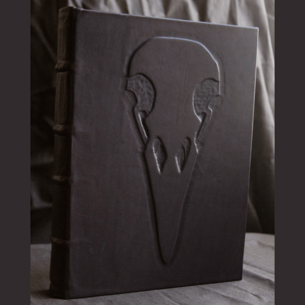 A dark purple leather bound book with an emboss of a crow's skull on the cover.