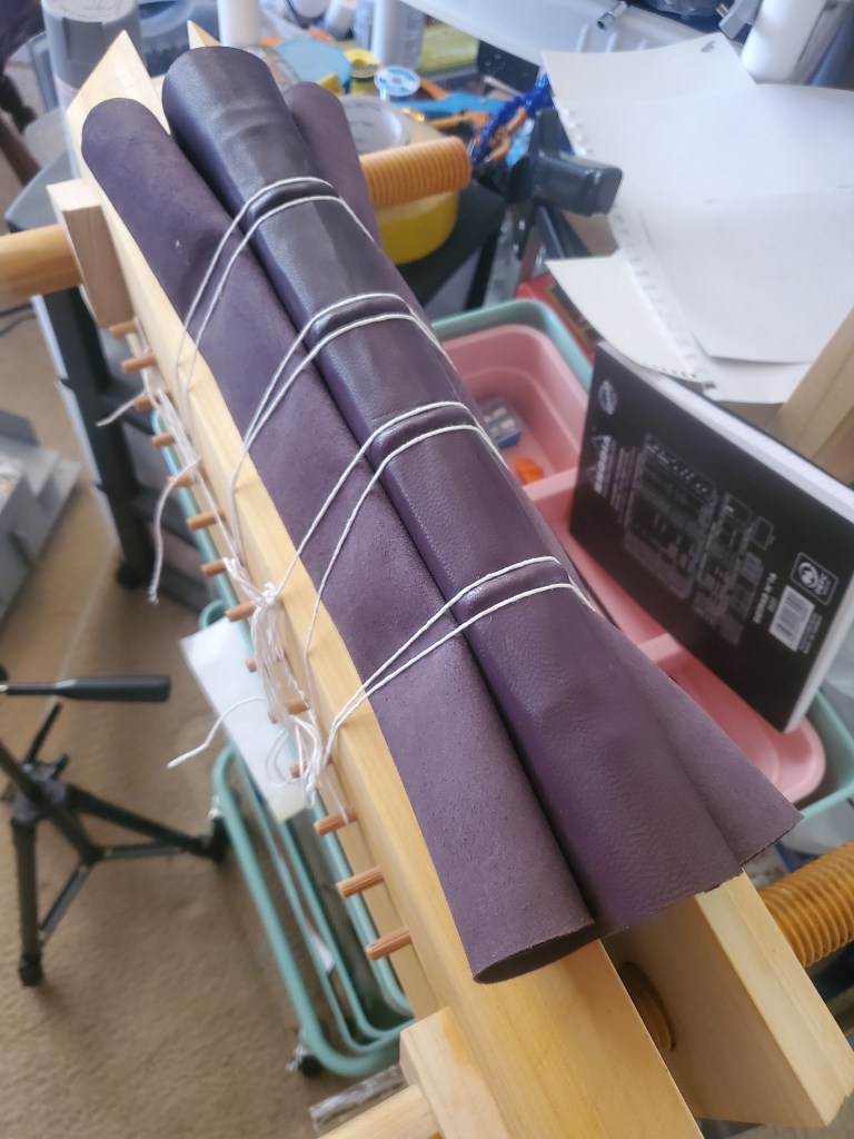 Book is pressed into lying book press, leather curled up and held onto the spine with twine.