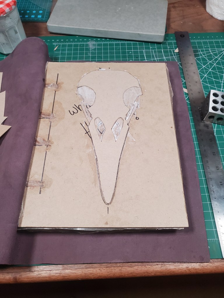 Raven skull cardstock layers are being glued to an unfinished book.